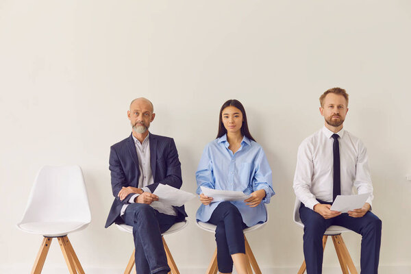 Three multiracial candidates of different ages sitting on chairs waiting for job interview