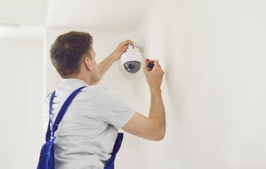 Üniformalı erkek teknisyen güvenlik kameralarını evin içine yerleştiriyor. Ofisteki ya da evdeki güvenlik kameralarını tamir ederken tornavida kullanıyor. Güvenlik sistemi ve güvenlik kavramı.