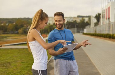 Kadın stajyer, erkek fitness koçuyla sohbet eder. Söz alışverişi eğitim deneyimini geliştirir, fitness hedeflerine ulaşmada iletişimin önemini vurgular.