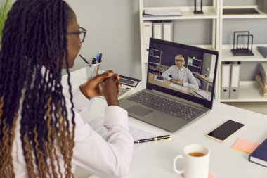 Afro-Amerikalı bir kadının laptop monitörüne baktığı iş yerindeki masada oturduğu ve erkek arkadaşlarıyla internet üzerinden ya da video konferans yaptığı görüntüler..