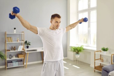 Beyaz tişört giyen, spor yapan ve dambıl kaldıran genç adamın portresi. Atletik adam el sıkışıyor. Spor, spor ve ev eğitimi konsepti.