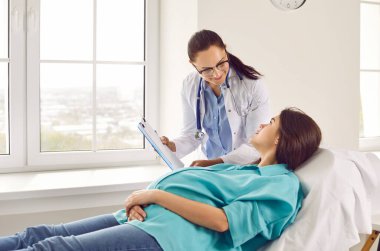 Hastanede ya da klinikte jinekoloğu ziyaret eden genç hamile bir kadın. Kadın doğum doktoru, kontrol sırasında hamilelik konusunda hastasına danışmanlık yapıyor..