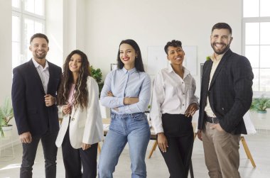 Modern ofiste ayakta duran ve poz veren, kendine güvenen ve başarı, birlik, profesyonellik, pozitif takım portresi ve insan ilişkileri sergilemek isteyen çeşitli mutlu profesyoneller.