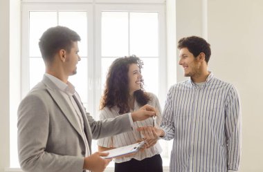 Yeni dairelerde gülümseyen genç bir çifte ev anahtarı veren bir emlakçının portresi. Başarılı bir aile ev sahibi olmaya hazır. Gayrimenkul piyasası ve taşınma kavramı.