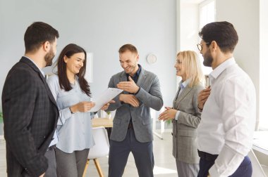 İş yerinde bir grup iş arkadaşı eğleniyor. Ofisteki bir grup insan bir arada durup komik bir şakaya gülüyorlar. İş, işyeri, arkadaşlık kavramı