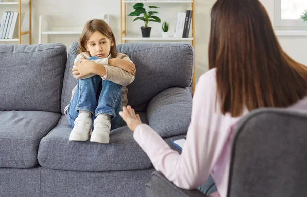 Psikolog ya da psikoterapist muayenehanesinde stres ve davranış problemi olan üzgün bir çocuk. Endişeli çocuk kanepede oturuyor kollarıyla dizlerine sarılıyor, kadın oğlanla konuşuyor. Danışmanlık kavramı