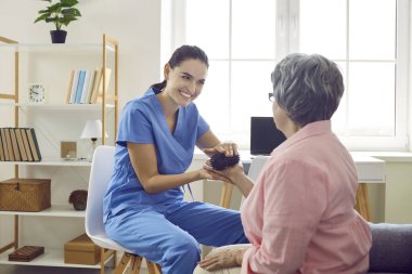 Dikenli topla yapılan alıştırmalar. Dost canlısı hemşire yaşlı kadına masaj yapmak için küçük masaj topları veriyor. Genç kadın bakıcı huzurevindeki yaşlı kadın hastayla ilgileniyor..