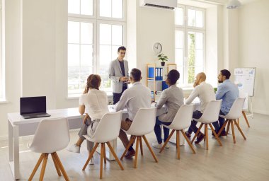 Çalışan sunum yapar ve yönetim kurulu üyelerine iş stratejisini açıklar. Ofisteki genç adam masada sıra sıra oturan iş adamları ve kadınların önünde konuşuyor. İş konsepti.