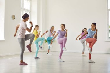 Çocuklar bir antrenörle spor yapıyor. Birkaç çocuk profesyonel bir eğitmenle spor egzersizleri yapıyor. Spor giyinen bir grup kız spor salonunda bir kadın öğretmenle birlikte.