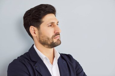 Kendine güvenen sakallı yakışıklı iş adamının resmi takım elbiseli portresi gri duvar arka planında tek başına duruyor ve yana bakıyor. İş portresi kavramı