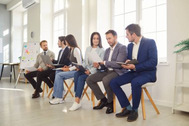 Ofis çalışanlarından oluşan bir ekip rahat koltuklarda oturuyor ve iş için önemli bir şey tartışıyorlar. Resmi kıyafetler giymiş modern teknolojiyi kullanarak. Ofis odasında iş ekibi var.