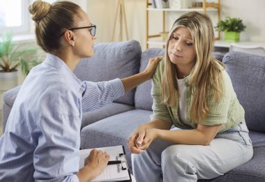 Empati ve destekle terapi seansı. Psikolog endişeli bir hastaya, nazik bir omuz dokunuşu ve özenli bir sohbete güven veriyor. Zihinsel sağlık desteği, güven ve bakım.