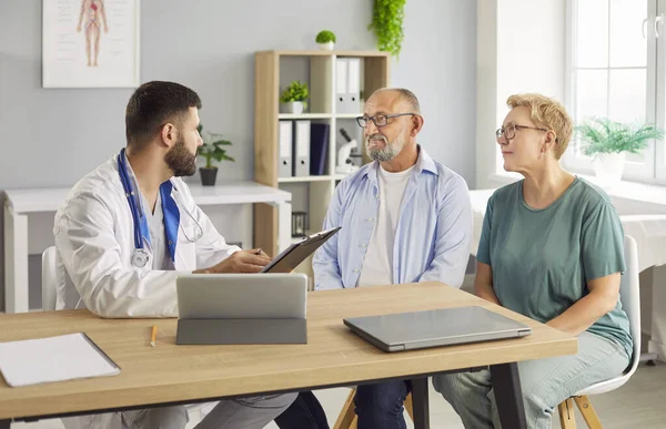 Doktor danışma klinikteki yaşlı çiftin tıbbi kayıtlarını inceler, sağlık testi sonuçlarını karşılar. Yaşlı, olgun hastalar doktorlarla tedaviyi tartışıyor. Tıp konsepti. 