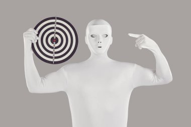 Beyaz tayt giyip beyaz bir maske takan ve elinde gri bir arkaplanda izole bir şekilde tuttuğu yuvarlak hedef tahtasını gösteren bir adamın portresi. Hedef kavramı