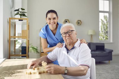 Arkadaş canlısı bakıcısı olan yaşlı bir adam Alzheimer ve bunamaya karşı hafıza eğitimi olarak bulmacaları çözüyor. Modern özel bakım evindeki yaşlı adam ve genç gülümseyen hemşire portresi..
