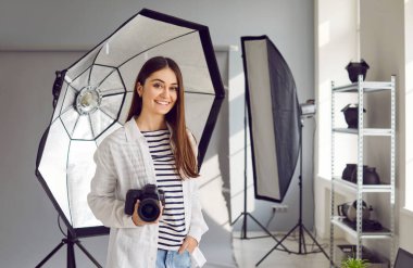 Fotoğraf stüdyosunda dijital fotoğraf makinesi olan genç bir kadın fotoğrafçı. Profesyonel DSR kameralı çekici bir genç kadın profesyonel fotoğraf makinesiyle stüdyoda duruyor.
