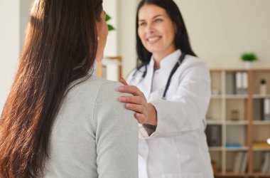 Gülümseyen dost canlısı genç bir doktorun portresi elini omzuna koyan kadın hastaya destek oluyor. Steteskop takan bir doktor klinikte muayene sırasında bir kadına danışmanlık yapıyor..