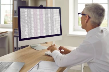 Ofisteki bilgisayarlarda çalışan bir adamın omuz üstü görüntüsü. İş adamı sayfa belgesinde PC tipi kullanır. İş yerindeki muhasebeci ya da finans müdürü. Finans, bankacılık kavramı.