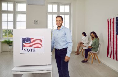 Mutlu gülümseyen Amerikalı seçmen portresi, seçim günü oy pusulasında kağıt oylarla kameraya bakıp, seçimini yapan ABD bayraklarıyla mutlu görünüyor..