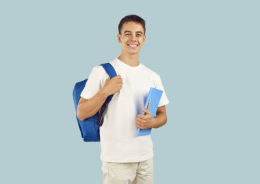 Mavi stüdyo arka planında izole edilmiş kameraya bakarak elinde kalem ve kitapla gülümseyen mutlu, kendine güvenen esmer çocuk portresi. Eğitim kavramı.