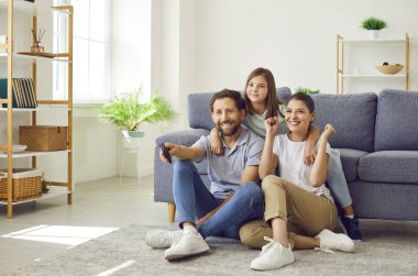 Heyecanlı mutlu bir aile, elinde uzaktan kumandayla televizyon izleyen bir kız çocuğu evdeki oturma odasında yerde oturuyor. Kızı olan aileler futbol takımını destekliyor..