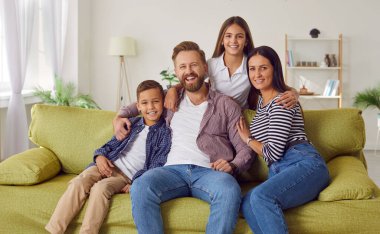 Ebeveynler ve çocuklar birlikte zaman geçiriyorlar. Evdeki kanepede dört kişilik mutlu bir aile. Neşeli, gülümseyen anne, baba, oğul ve kızın portresi yeşil kanepede oturuyor.