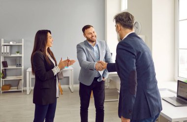 Ofiste tokalaşan iki gülümseyen erkek iş ortağı. Patron, ekip lideri personel toplantısında mutlu erkek çalışanlarla tokalaşıyor. Saygı gösteriyor, selamlıyor.