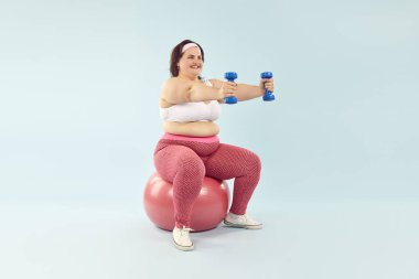 Artı, halterli, iyimser, genç kadın eğitimi. Aşırı kilolu, spor giyim ve saç bandı takan şişman bir kadın spor salonunda oturmuş halterlerle arka planda egzersiz yapıyor. Kilo kaybı, motivasyon