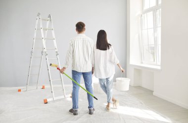 Evli genç bir çift yeni bir ev onarımı planlıyor, mutlu koca ve eş iç dekorasyondan zevk alıyor, duvarda çizimler yapıyor, birlikte resim yapıyor, mutlu aile hayatı için ev dekorasyonu yapıyor. 