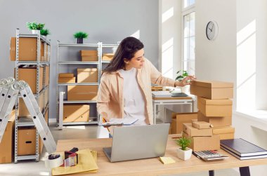 Depoda karton kutuların arasında çalışan kendine güvenen genç bir bayan çalışan. İşyerindeki stokları ve envanterleri kontrol eden bir kadın. Küçük işletme sahibi depoda müşteri için sipariş hazırlıyor.