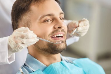 Diş muayenesi sırasında hasta oturur, çünkü dişçi doktor muayene için bir cihaz kullanır. Kliniği ziyaret ederek, diş sağlığı ve profesyonel diş hekimliği hizmetlerinin önemini vurgulayın.