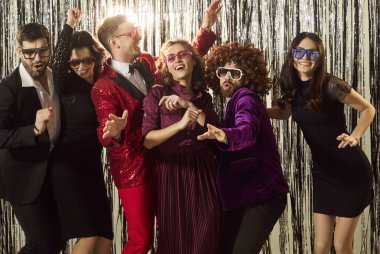 Parti toplama, arkadaşlar poz verme, dans etme, neşeli parti gözlükleri ve parlak şenlik kıyafetleri giyme, pırıl pırıl gümüş parıldayan süsler, parlak ışıklar, neşeli parti mutluluğu, sevinç kutlamaları.