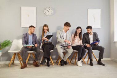 Bir grup iş adamı ellerinde panolarla sandalyelere oturup sohbet ediyor ve kağıtları kontrol ediyorlar. Röportaja ya da iş toplantısına hazırlanan gülümseyen profesyoneller, düşüncelerini paylaşıyor ve özgeçmişlerini gözden geçiriyorlar.