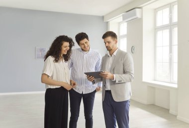 Kendine güvenen genç profesyonel emlakçının portresi modern yeni apartman dairesinde birkaç müşteriyle birlikte emlak satın alma sözleşmesini tartışıyor. Taşınma, kira ve emlak piyasası kavramı.