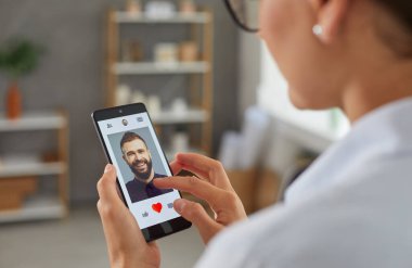 Kadın akıllı telefon ekranındaki mobil flört uygulamasında erkeklere benzer bir fotoğraf verecek. İnternette aşk ve ilişki arayan bekar bir kadın. Sosyal uygulama kavramında romantik partner aranıyor.