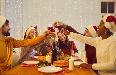 Gülümseyen çok ırklı arkadaşlar masa başı kadehlerinde oturup bayramları Noel yemeğiyle kutluyorlar. Lezzetli yiyecekler yiyen farklı etnik çeşitlilikte genç insanlar yeni yıl kutlaması için toplanıyor..