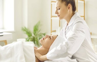 Güzellik salonunda ya da kozmetoloji dolabında gözleri kapalı yatan genç bir kıza omuz ve boyun masajı yapan kadın masörünün yan görüntüsü. Kozmetik uzmanı kaplıcadaki kadına masaj yapıyor..