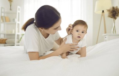 Küçük kızımla sabah rutini. Genç ve sevgi dolu anne altı aylık güzel kızıyla sabahları evde vakit geçiriyor. Anne ve bebek beyaz yatakta birlikte uzanırlar..