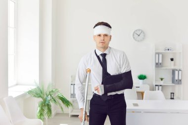 İş yerinde koltuk değneği üzerinde kırık bir kol ve bandajla kazadan sonra yaralı bir işadamının tam boy portresi. Ciddi fiziksel kaza sonrası rehabilitasyon kavramı.