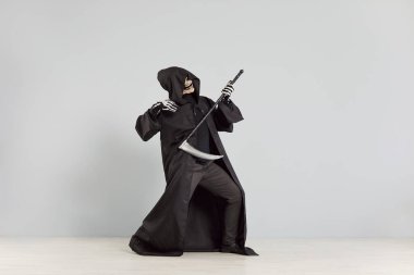 Komik ölüm meleği gri bir zeminde dururken gitar gibi tırpan çalıyor. Cadılar Bayramı temalı partide müzik ve ölüm unsurlarını birleştiren maskeli bir iskelet yer alıyor..