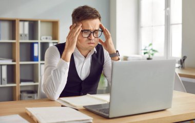 Uzun saatler çalıştıktan sonra iş yerindeki masasında oturan ve baş ağrısından muzdarip yorgun ve yorgun iş adamının portresi. Aşırı çalışma, stres konsepti.