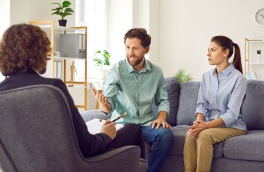 Genç evli çift koltukta oturup psikologla konuşuyor ve danışmanlık bürosunda sorun ve çözüm bulmaya çalışıyorlar. Aile terapisi, ilişki ve akıl sağlığı konsepti.