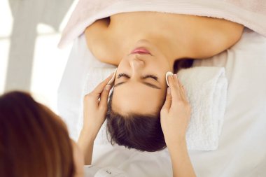 Doktor kozmetik operasyonlarını kozmetik kliniğinde gerçekleştiriyor. Kadın kozmetikçi, estetik ameliyatlardan önce hastaları pamuk pedlerle siliyor. Kanepede gözleri kapalı yatan kadın manzarası..