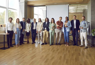 Çeşitli etnik çeşitlilikteki iş dünyasının, kameraya bakıp gülümseyen kadın ve erkeklerin tam boy portresi. Mutlu şirket çalışanları ya da ofiste duran bir grup personel..