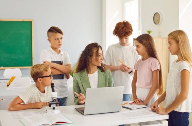 Ciddi okul fen bilgisi öğretmeni bir grup çocuk öğrenciyle iletişim kurar, güvenilir bilgilerin nasıl aranacağı ve yazılacağı konusunda tavsiyelerde bulunur, hataları düzeltir ve sınav sınavına hazırlanır