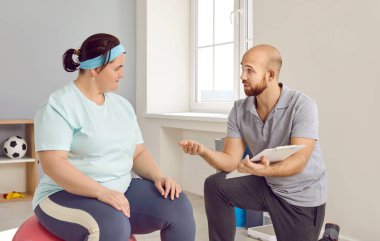 Artı boy, obez kadın fitness eğitmeniyle fitness programı hakkında konuşuyor. Spor giyim sektöründe kilo vermek için spor salonunda çalışan şişman, genç bir kadın. Kilo kaybı, sağlıklı yaşam tarzı.