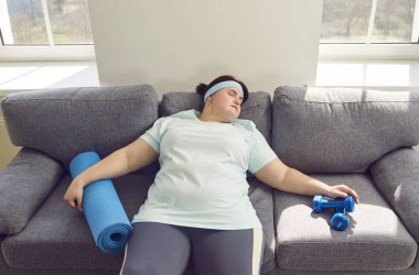 Spor kıyafetleri giyip spor kıyafetlerini giyip, evdeki kanepede dinlenen şişman, komik bir kadının portresi. Spor, spor ve vücut pozitif konsept.