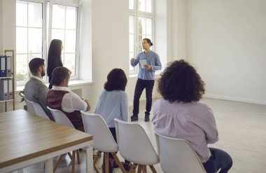 Motive olmuş erkek konuşmacı ya da koç konuşması ofis odasındaki çeşitli izleyiciler için sunum yapıyor. Kendinden emin sunucu eğitmeni dinleyicilerin önünde konuşur, eğitime motivasyon eğitimi verir..