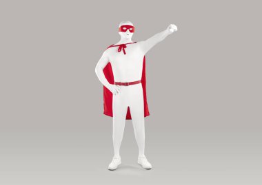 Beyaz tayt giymiş, kırmızı pelerinli, yüzü tanınmayan bir adamın tam boy portresi. Süpermen pozu vermiş. Stüdyo gri arka planda el ele duruyormuş..