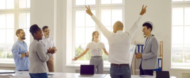 Mutlu, neşeli insanlardan oluşan bir ekip iş başarısını kutluyor. İş arkadaşları ofis masasının etrafında durup alkışlarken heyecanlı genç adam ellerini kaldırıyor. Sancak, başlık arkaplanı